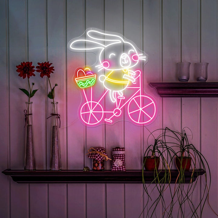 Bunny on Bike Easter LED neon sign glowing on wall with playful bunny riding a bike design for home decor, nursery, party, or shop display by Neon.Shop.