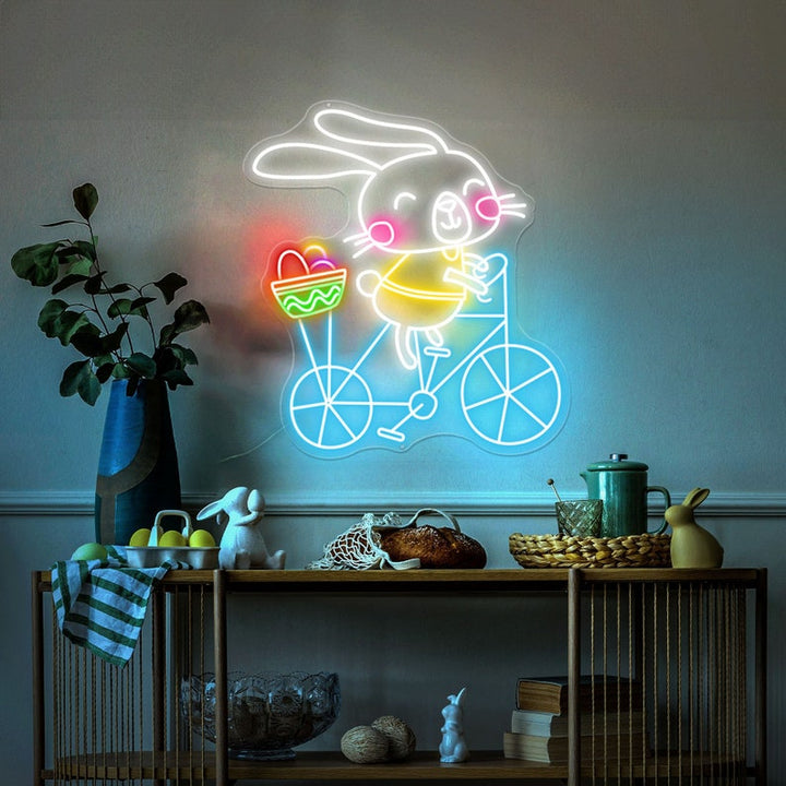 Bunny on Bike Easter LED neon sign glowing on wall with playful bunny riding a bike design for home decor, nursery, party, or shop display by Neon.Shop.