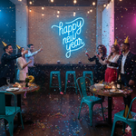 Bright Happy New Year LED neon sign in modern script font, glowing against a dark brick wall by Neon.Shop.