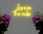 Love On The Rocks Valentine’s Day LED neon sign glowing in bold romantic tones, perfect for bedroom décor, home bars, Valentine’s gifts, and playful love-themed spaces by Neon.Shop.